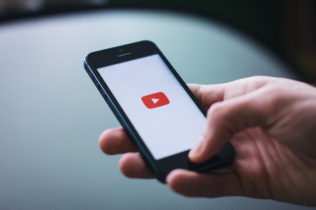 A person holding a smartphone with the YouTube logo on the screen, symbolizing how to use YouTube to market your business.